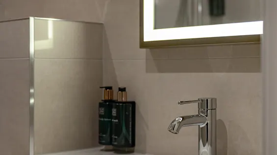 Et moderne badeværelse med håndvask, armatur og oplyst spejl. Toiletartikler står på bordet.
