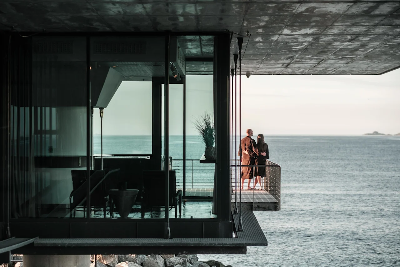 Two people on a balcony at Farris Bad, looking out at the vast, calm sea.