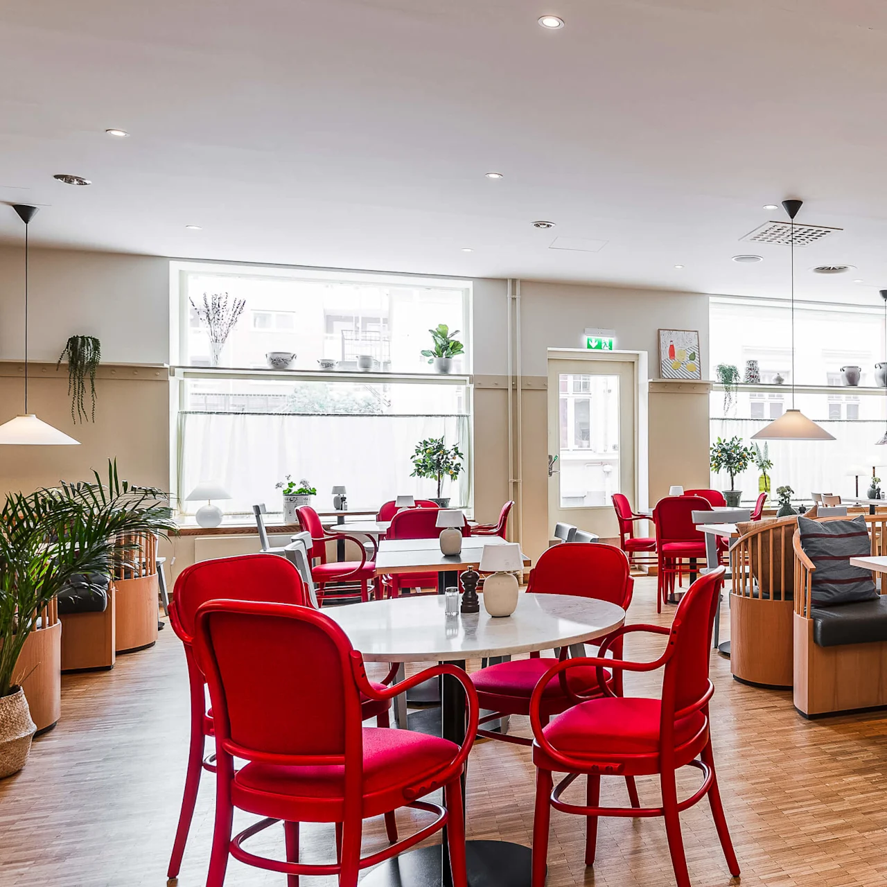 Ett ljust och rymligt caféinteriör med röda stolar, träbord, hänglampor och dekorativ konst på väggarna.