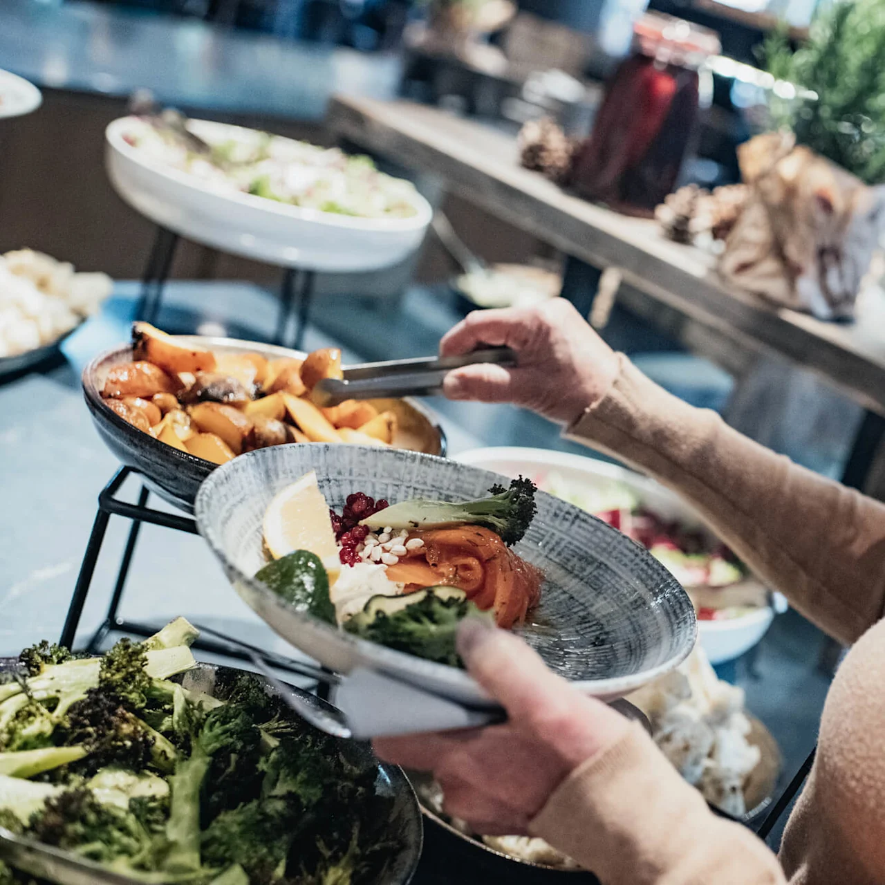 A person serving themselves at a buffet with a variety of dishes, focusing on adding food to their plate.