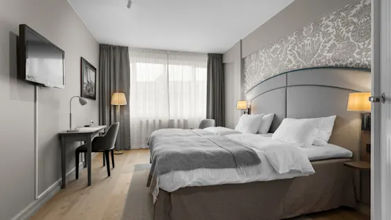 An inviting hotel room with twin beds, a dedicated workspace, and a television, providing a relaxing and productive environment.