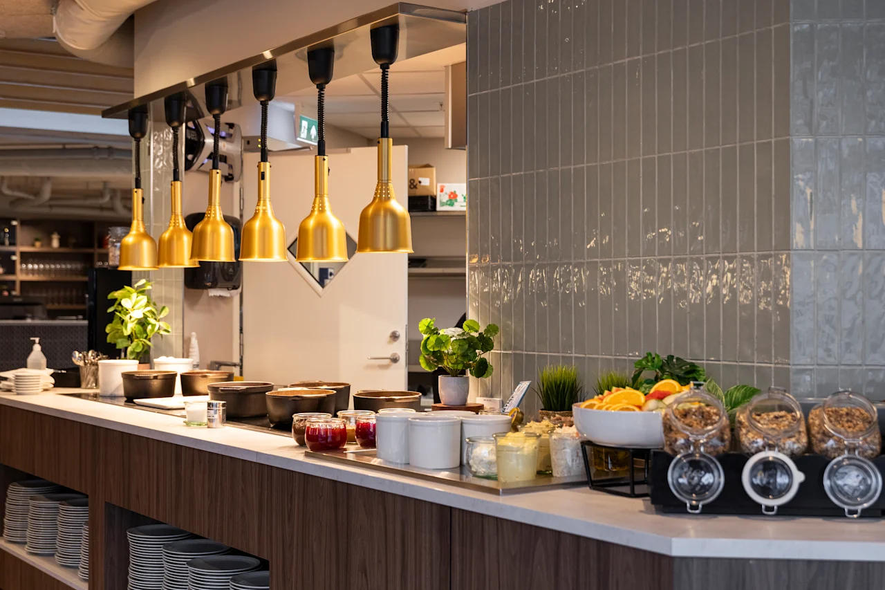 A welcoming buffet spread with golden lamps illuminating a variety of breakfast items like fresh fruit, yogurt, and granola.