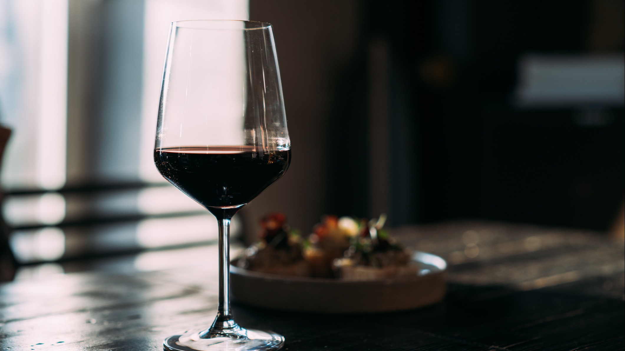 Et glas rødvin ved siden af en tallerken ved et vindue. 