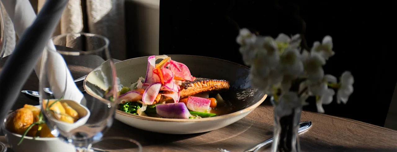 A beautifully plated meal featuring fish and colorful vegetables on a set dining table, ready for a pleasant dining experience.