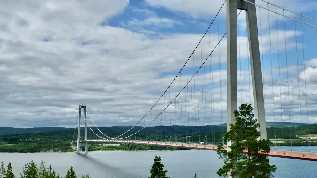 Kaunis näkymä suuresta riippusillasta, joka ylittää laajan vesistön, vihreiden metsien ympäröimänä. Höga kusten and Sundsvall.