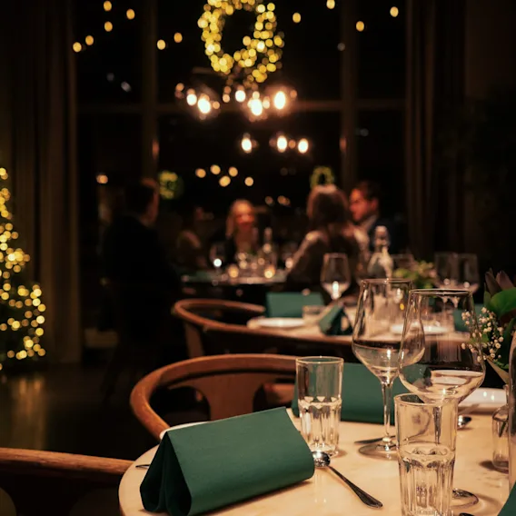 Koselig restaurant dekket til middag med varm julebelysning og gjester i bakgrunnen