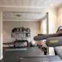 Et løbebånd står foran flere fitnessudstyr som kettlebells og en balancebold i et lyst træningsrum. På væggen står der: "THE ONLY PERSON YOU NEED TO BE BETTER THAN IS THE PERSON YOU WERE YESTERDAY."