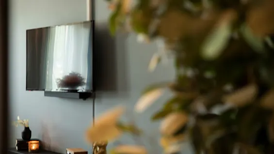 En koselig interiørscene med en veggmontert TV som reflekterer et vindu, og en hylle med dekorative gjenstander under.