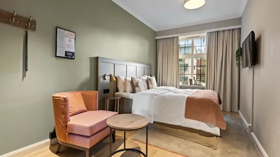 Et koselig hotellrom på Home Hotel Gabelshus med en komfortabel seng, en lenestol og et vindu med utsikt over utsiden.