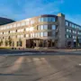 Et grått steinhotell med teksten "Skifer Hotel" er opplyst av sollys. Det står på et gatehjørne med et fjell og blå himmel i bakgrunnen.