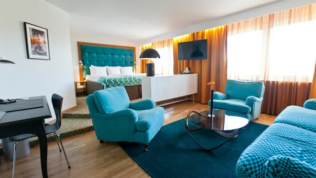 Siisti, moderni hotellihuone, jossa on suuri sänky, turkoosi nojatuoli ja pieni pöytä. Tilassa on seinälle kiinnitetty TV, työpöytä ja runsaasti luonnonvaloa suurista ikkunoista.