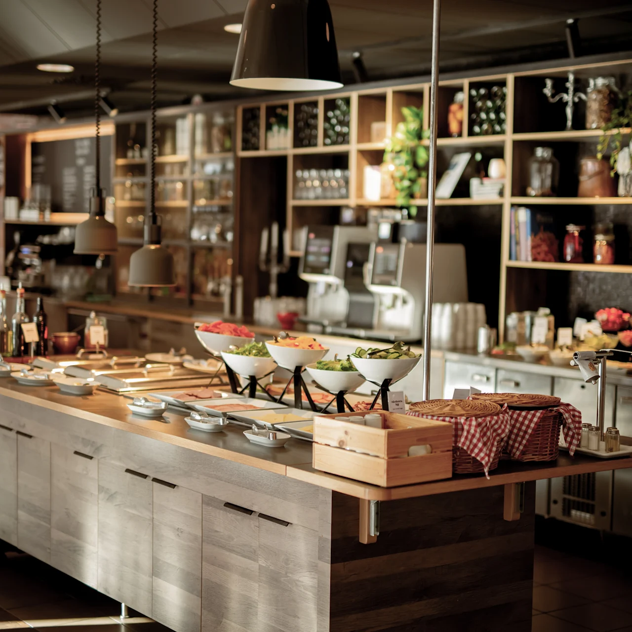Buffet counter displaying various salad bowls on a wooden table; surrounded by hanging lamps in a warmly lit restaurant environment.