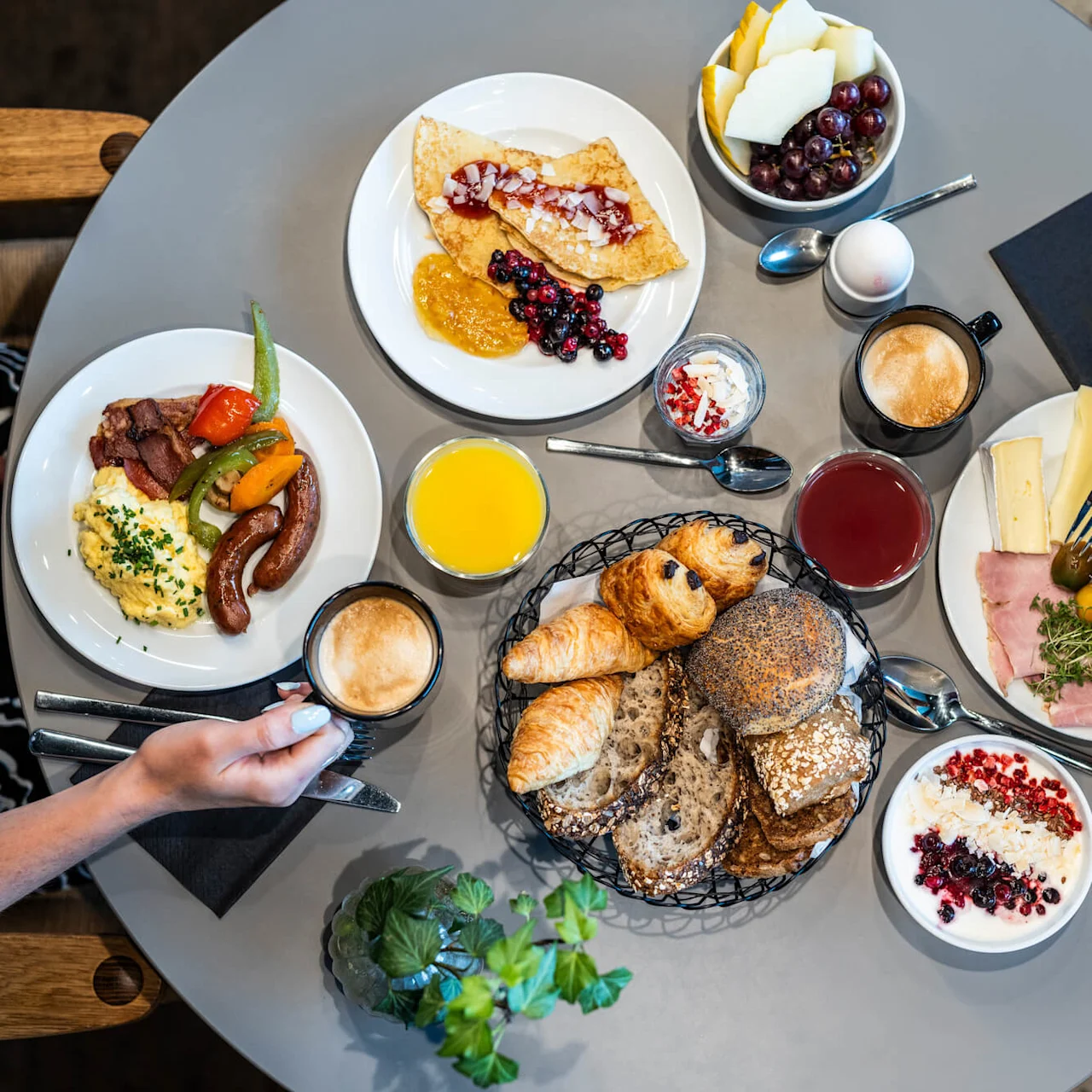 Et oversiktsbilde av et vakkert dekket frokostbord med ferskt brød, croissanter, yoghurt med bær, eggerøre, pølser, ost, ferske grønnsaker, juice, kaffe og frukt.