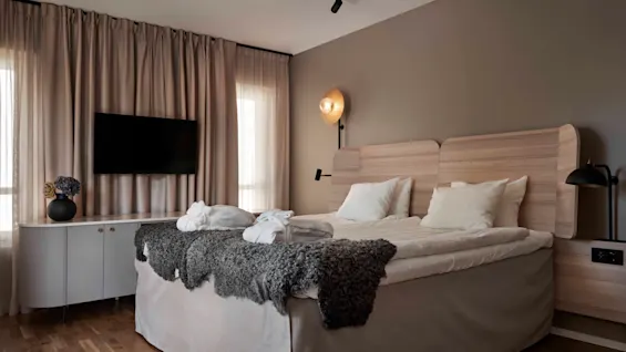 Ett modernt och inbjudande hotellrum med en stor säng, badrockar, en väggmonterad TV och varm belysning.