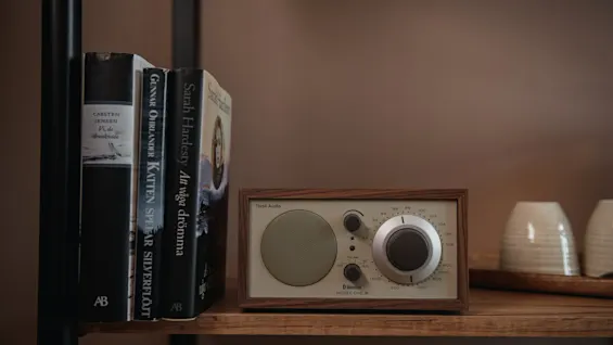 A vintage-style radio with dials and switches, labeled "Tivoli Audio" and "Model One," rests on a wooden shelf next to three books and two ceramic cups.