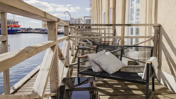 En indbydende balkon ved vandet med en hyggelig bænk og puder, der tilbyder fredfyldt udsigt over havnen.