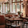 A warm and inviting restaurant interior with tables, chairs, plants, and soft lighting, creating a cozy atmosphere.