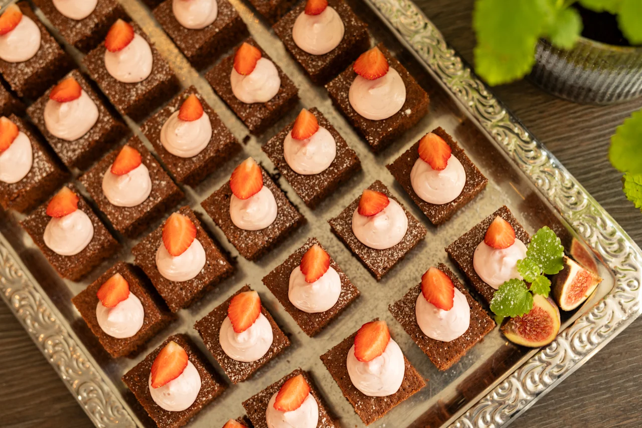 Läcker chokladdessert i fyrkantig form med jordgubbsgrädde och färsk frukt på en utsmyckad silverbricka, redo att serveras.
