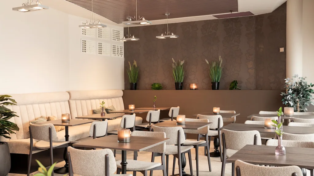 Viihtyisä ravintolaruokailutila, jossa on paljon pöytiä kynttilöineen, valmiina vieraille.