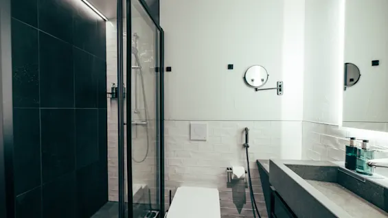 A modern and clean bathroom featuring a walk-in shower with dark tiles, a toilet, and a stylish concrete sink.