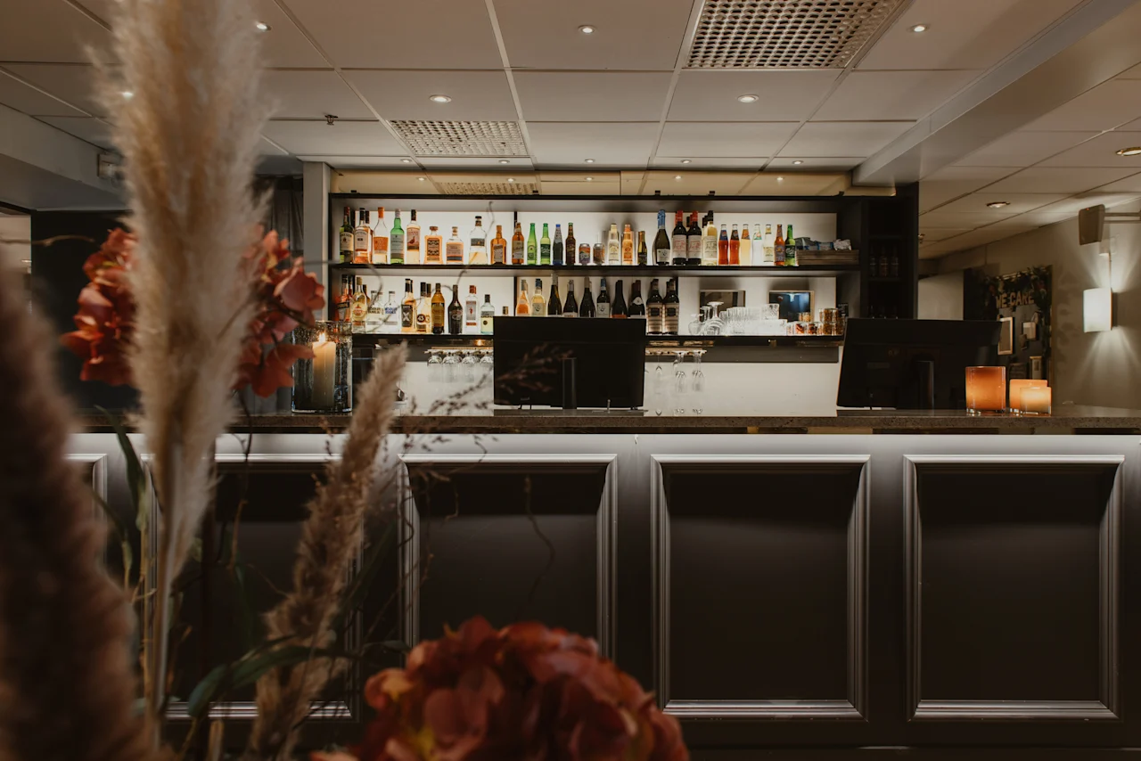A cozy bar area at Home Hotel Kung Oscar, featuring a well-stocked shelf of bottles and a warm, inviting ambiance. 🥂