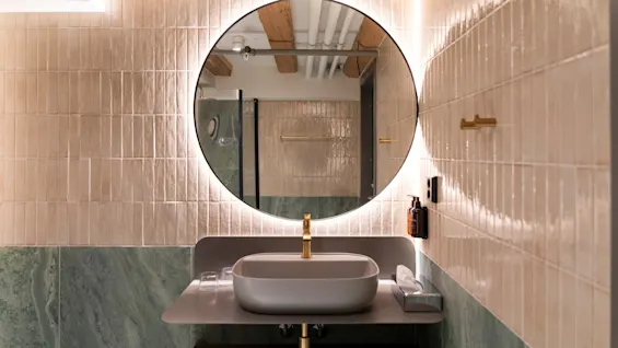 Et moderne baderomsmiljø med elegant servant, gullkran og stort, bakgrunnsbelyst speil, perfekt for daglige rutiner.