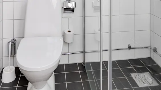 A bathroom with a white toilet, towels, and a shower stall, with tiled walls and a black tiled floor.
