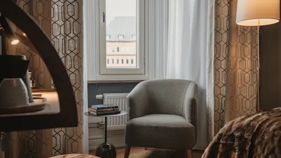 Home Hotel Baltzar - Compact Single. A welcoming hotel room with a comfortable armchair, books, and a window view.