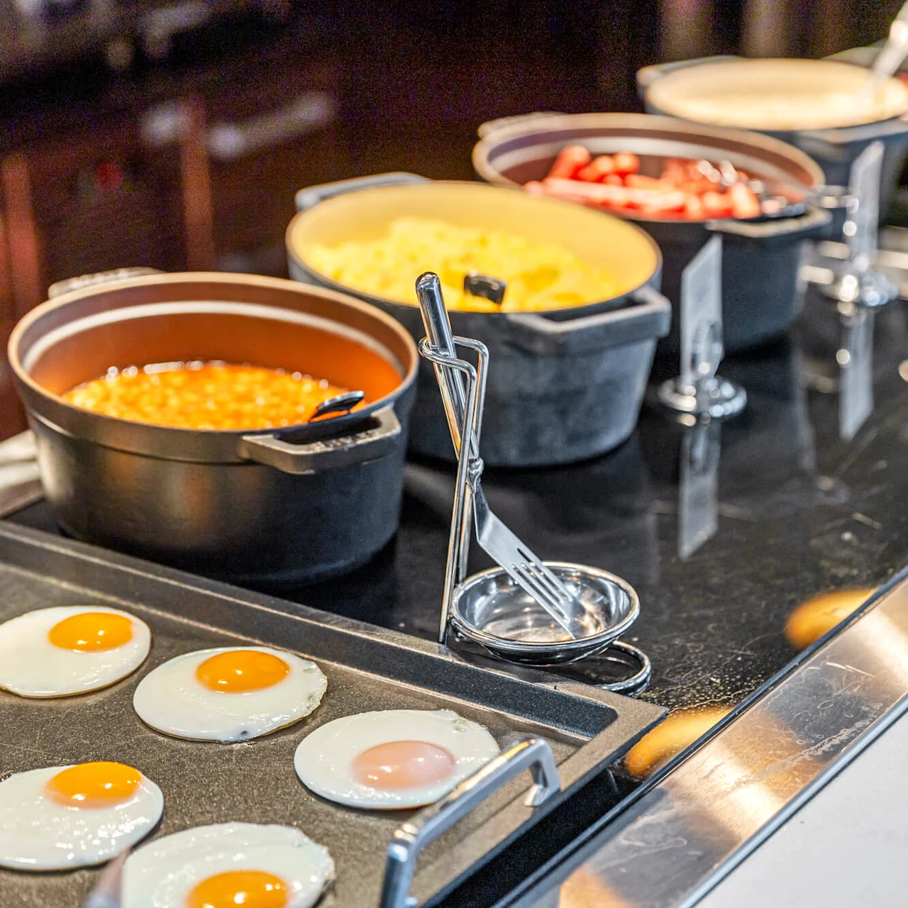 A buffet with eggs frying on a griddle and pots of beans, cheese, and sauces, in a kitchen.