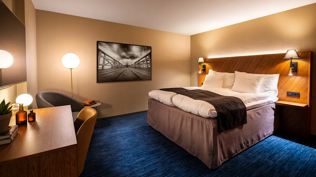 A well-lit hotel room with a neatly made bed, artwork, and furnishings in a contemporary style.