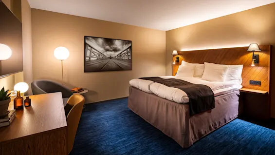 Ett välbelyst hotellrum med en prydligt bäddad säng, konstverk och möbler i en samtida stil.