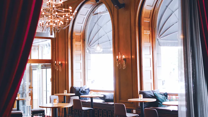 Elegant café interior with chandelier, arched windows, and cozy seating area bathed in natural light.