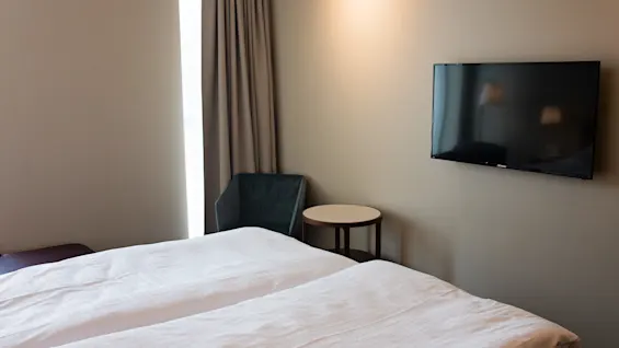 Mukava hotellihuone, jossa kaksi sänkyä, seinälle asennettu televisio ja pieni pöytä tuolineen.