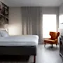 Ett ljust och inbjudande hotellrum med en bekväm säng, en mysig fåtölj och en funktionell skrivbordsplats.