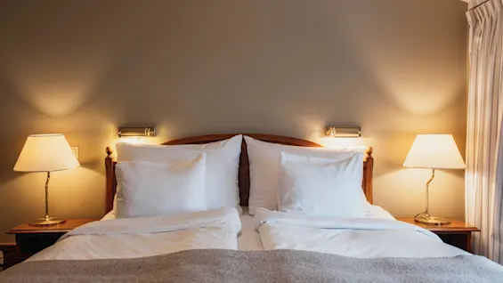 Ett mysigt hotellrum med en bäddad säng, två sänglampor och varm belysning, som inbjuder till en vilsam vistelse.