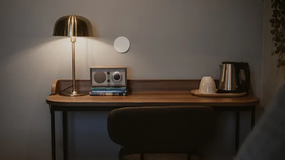 Ett mysigt hotellrumsskrivbord med en varm lampa, en radio och en teuppsättning, inbjudande till avkoppling eller arbete.