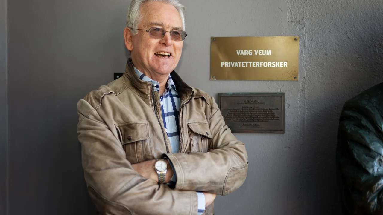 Gunnar Staalesen standing in front of plate on wall in Bergen. 
