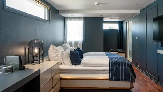 Et moderne og innbydende hotellrom med en komfortabel seng med blå detaljer, et elegant nattbord og varmt tregulv.