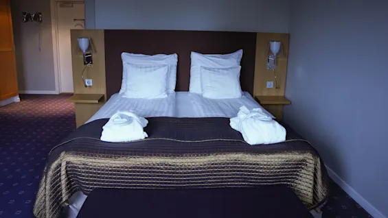 A double bed with pillows and folded towels, neatly arranged in a hotel room.
