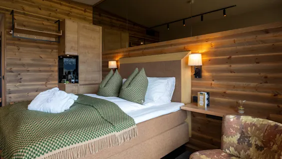Ett mysigt hotellrum på Skarsnuten med en säng, träväggar, varm belysning och en badrock, inbjudande till avkoppling.