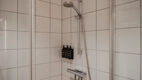 En ljus och inbjudande hotell dusch med vita kaklade väggar, ett krom duschhuvud och praktiska väggmonterade toalettartiklar.