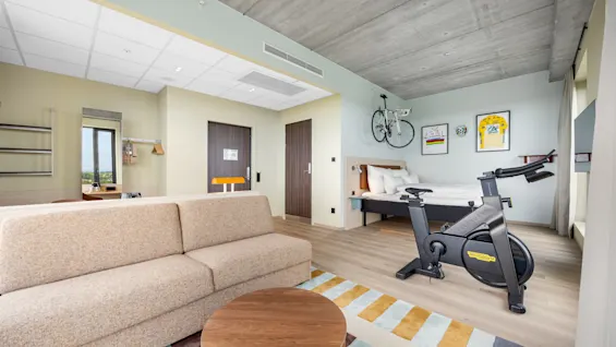 A modern hotel room with a comfortable sofa, a bed, and a stationary exercise bike for guests to stay active.