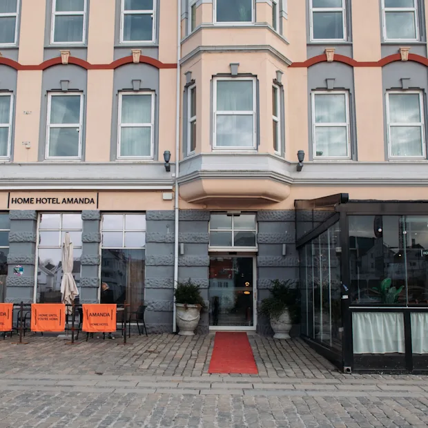 En charmerende bygning med skiltet HOME HOTEL. Rød løber til indgangen, med udendørs siddepladser og et indglasset område.