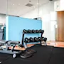 Vektbenk og håndvekter er satt opp i et treningsstudio. Tre vektskiver ligger på gulvet. Tekst på veggen sier "STRONGER - FASTER - BETTER."