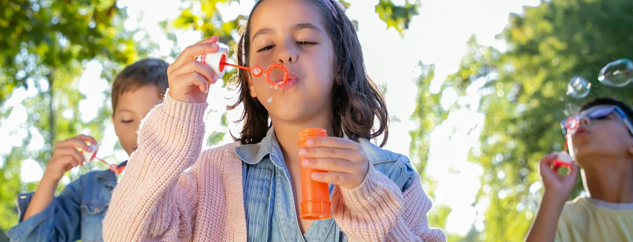 Children joyfully blowing bubbles outdoors on a sunny day, creating a playful and lighthearted scene.