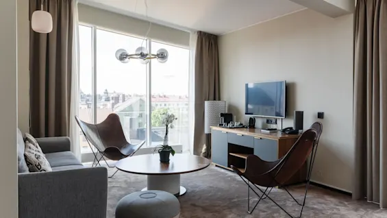 Modernt vardagsrum med soffa, soffbord och stolar, stort fönster, tv och skrivbord, inredningsdesign.