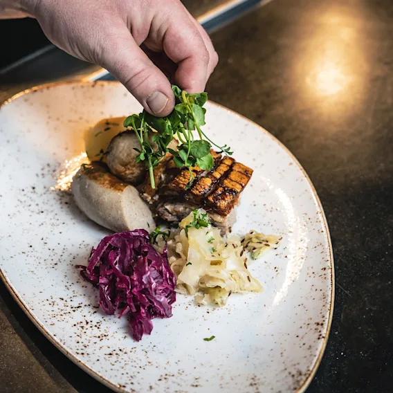 Hender som pynter en tallerken med tradisjonell julemat bestående av ribbe, pølse og surkål.