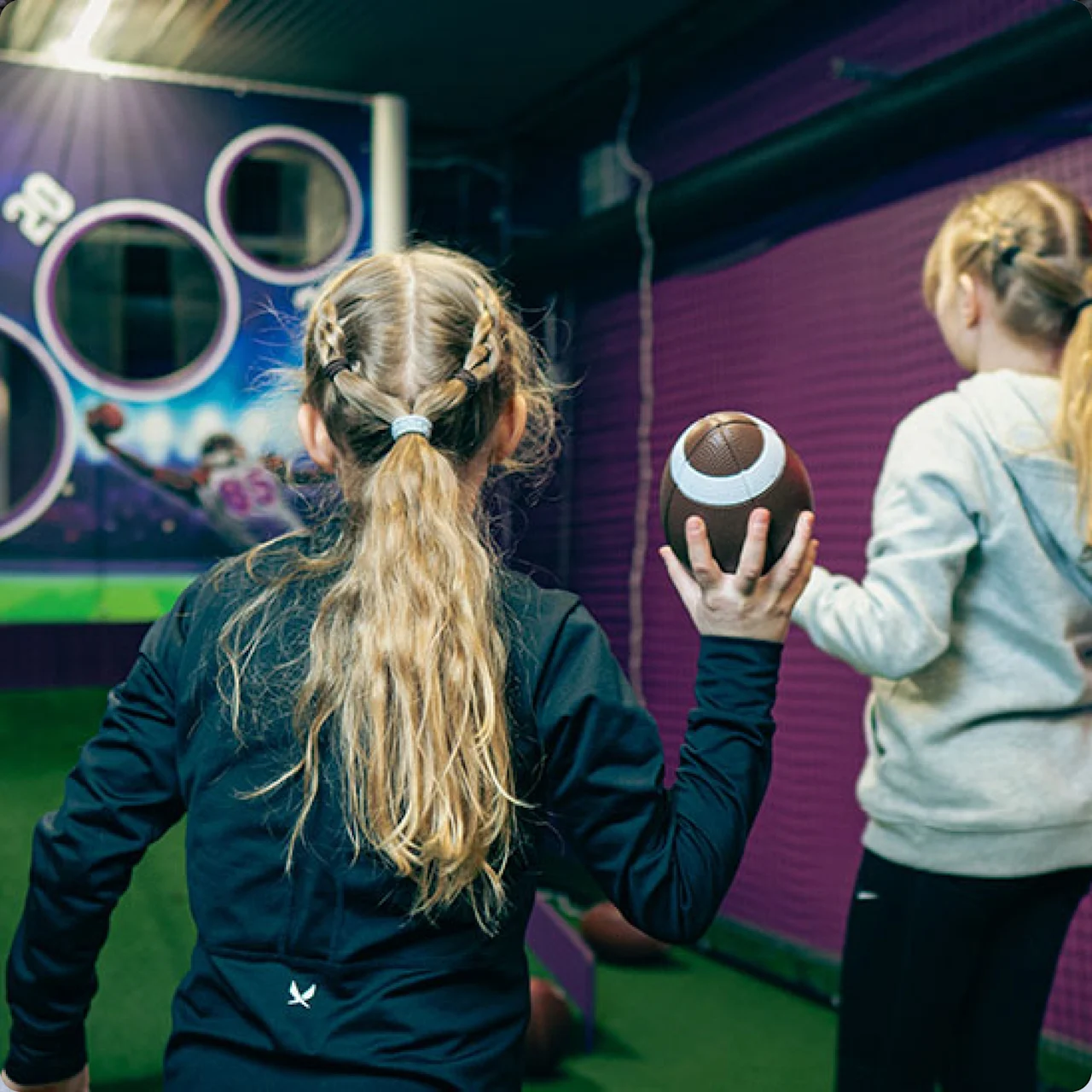 Kaksi lasta pelaa sisäjalkapallopeliä. Toinen pitää palloa ja katsoo maalitaulua, jossa on ympyrät ja 20.