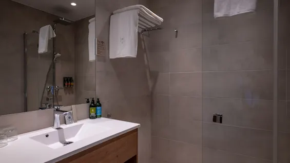 Ett rent och modernt hotellbadrum med handfat, spegel och duschutrymme med fräscha handdukar.