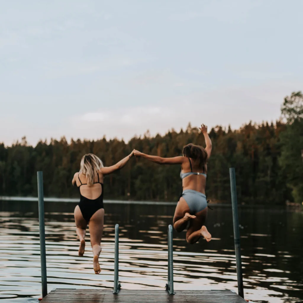Två tjejer hoppar ner i en sjö från en brygga i Sverige.